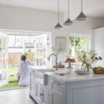 White Original kitchen design and soft grey kitchen island infront of open white French doors overlooking the garden