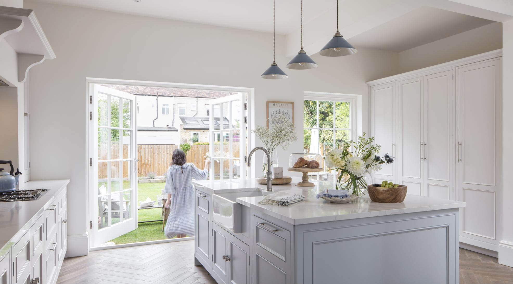White Original kitchen design and soft grey kitchen island infront of open white French doors overlooking the garden