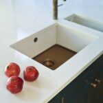 White kitchen island worktop with white sink featuring a brass base and tap