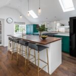 Bold green Shaker kitchen cabinetry with white kitchen island featuring walnut worktop and gold and dark grey bar stools