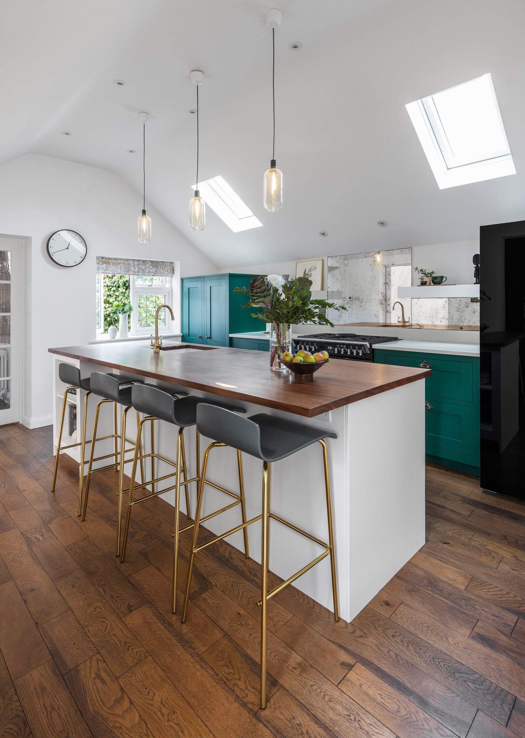 Bold green Shaker kitchen cabinetry with white kitchen island featuring walnut worktop and gold and dark grey bar stools