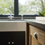 Closeup of oak kitchen island drawer with silver handle in front of black cabinetry with white basin sink