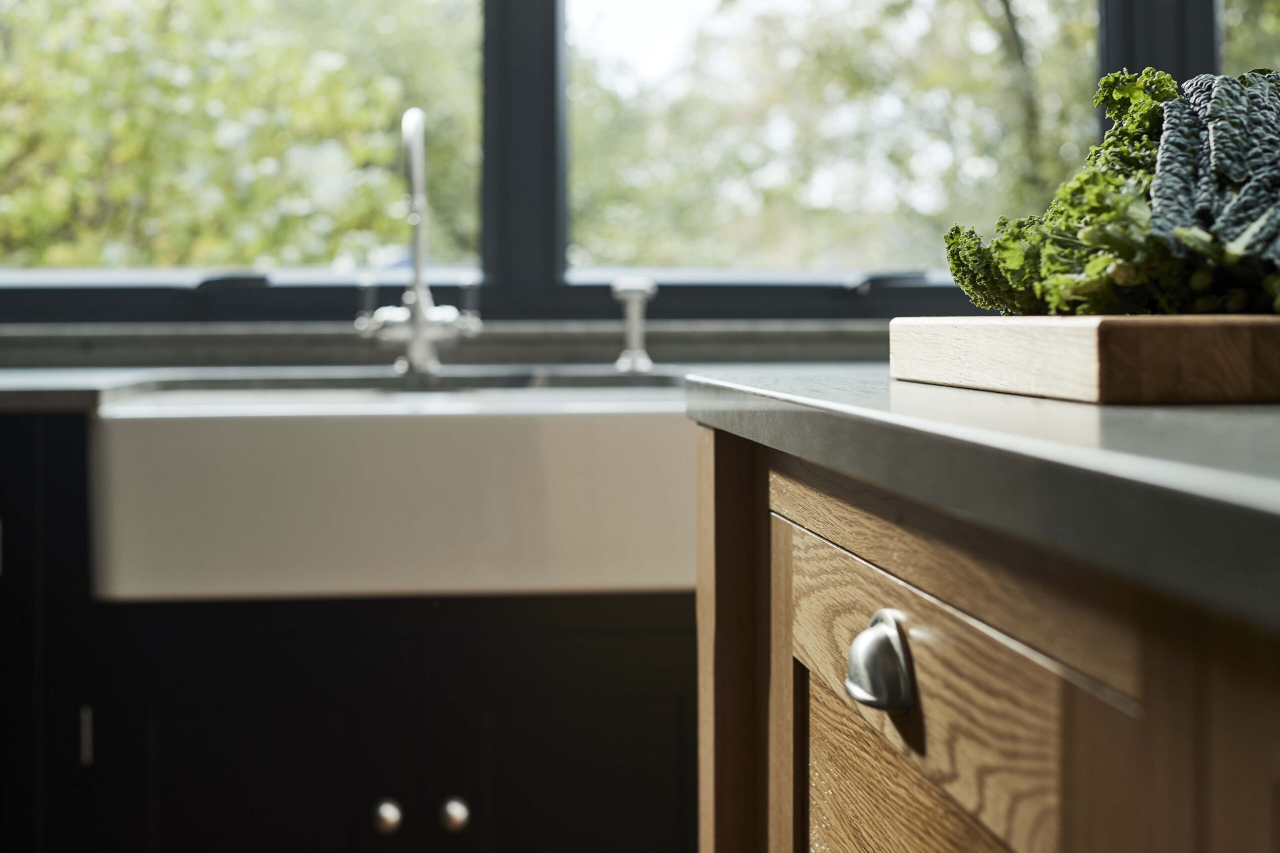 Closeup of oak kitchen island drawer with silver handle in front of black cabinetry with white basin sink