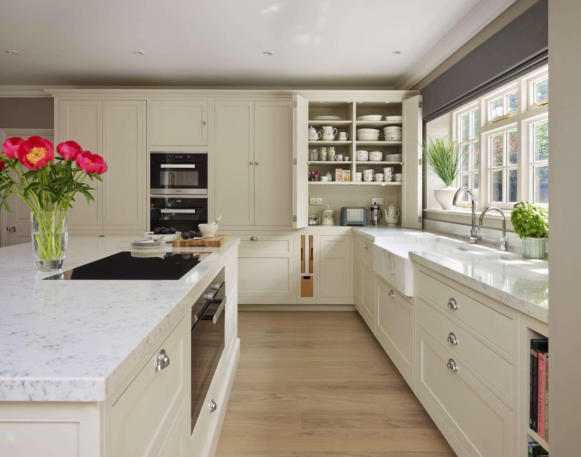 Tall beige Original kitchen cabinetry with integrated appliances open to reveal organised storage