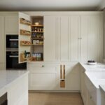 Tall beige Original kitchen cabinetry with integrated appliances open to reveal organised storage