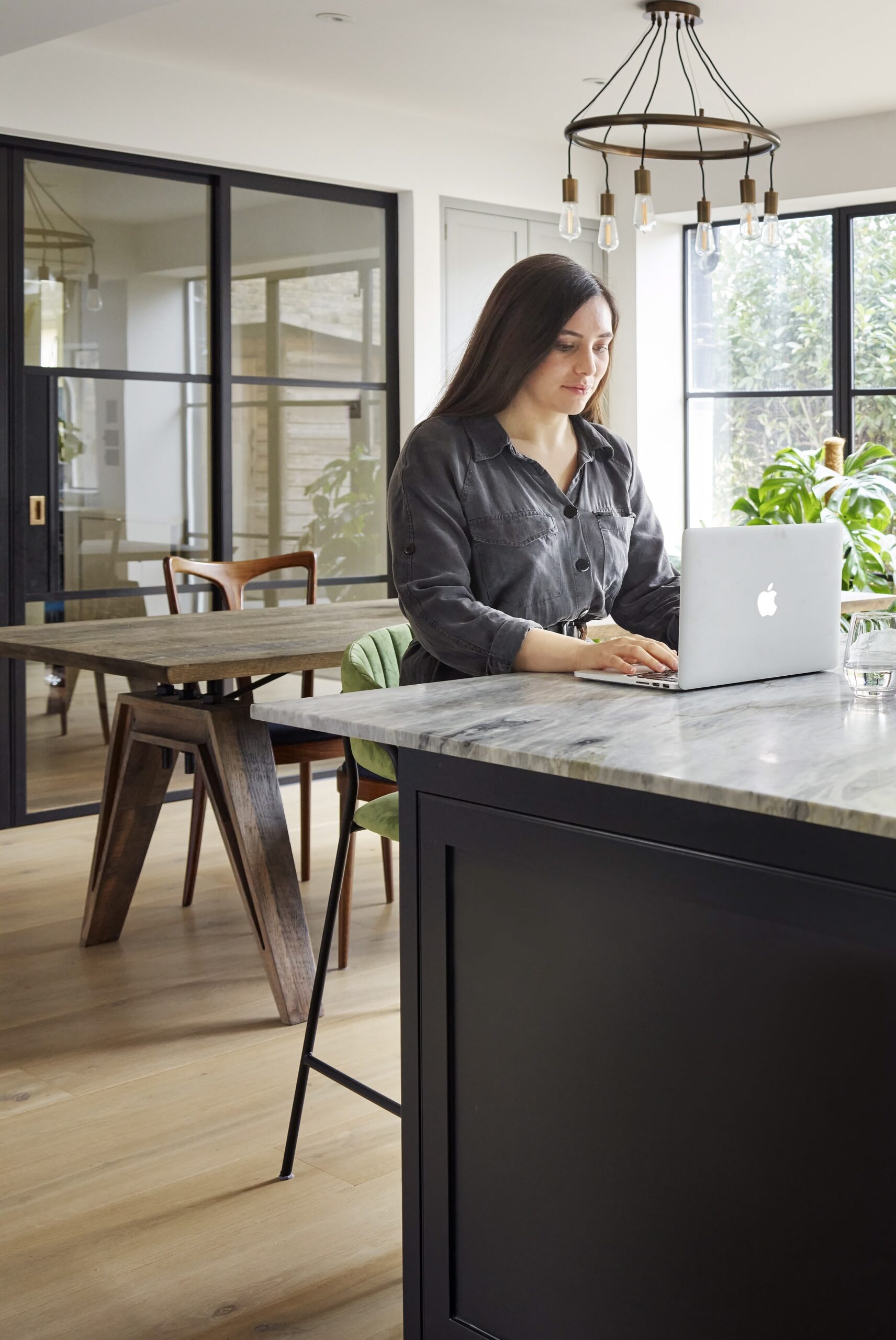 Woman on a laptop sat against a dark kitchen island with marble worktop