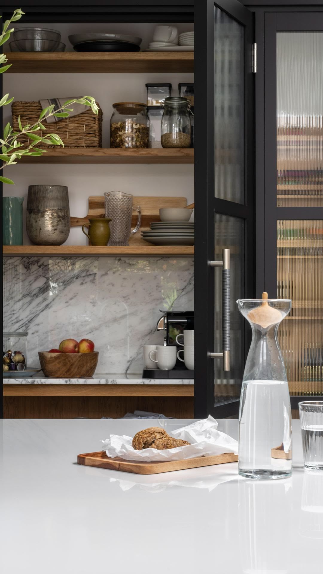 Black pantry larder with glass doors open to show organised storage