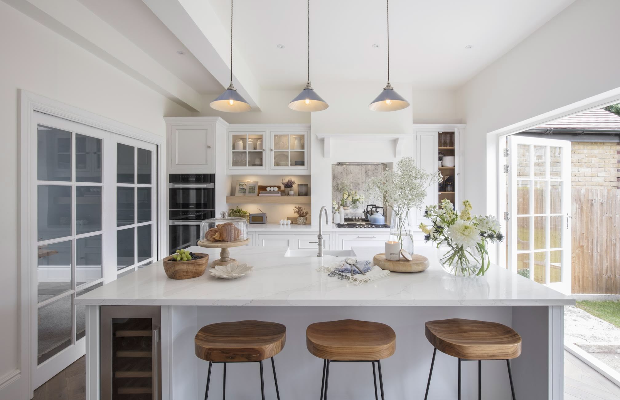 White kitchen island with white worktop featuring wine fridge and wooden bar stools
