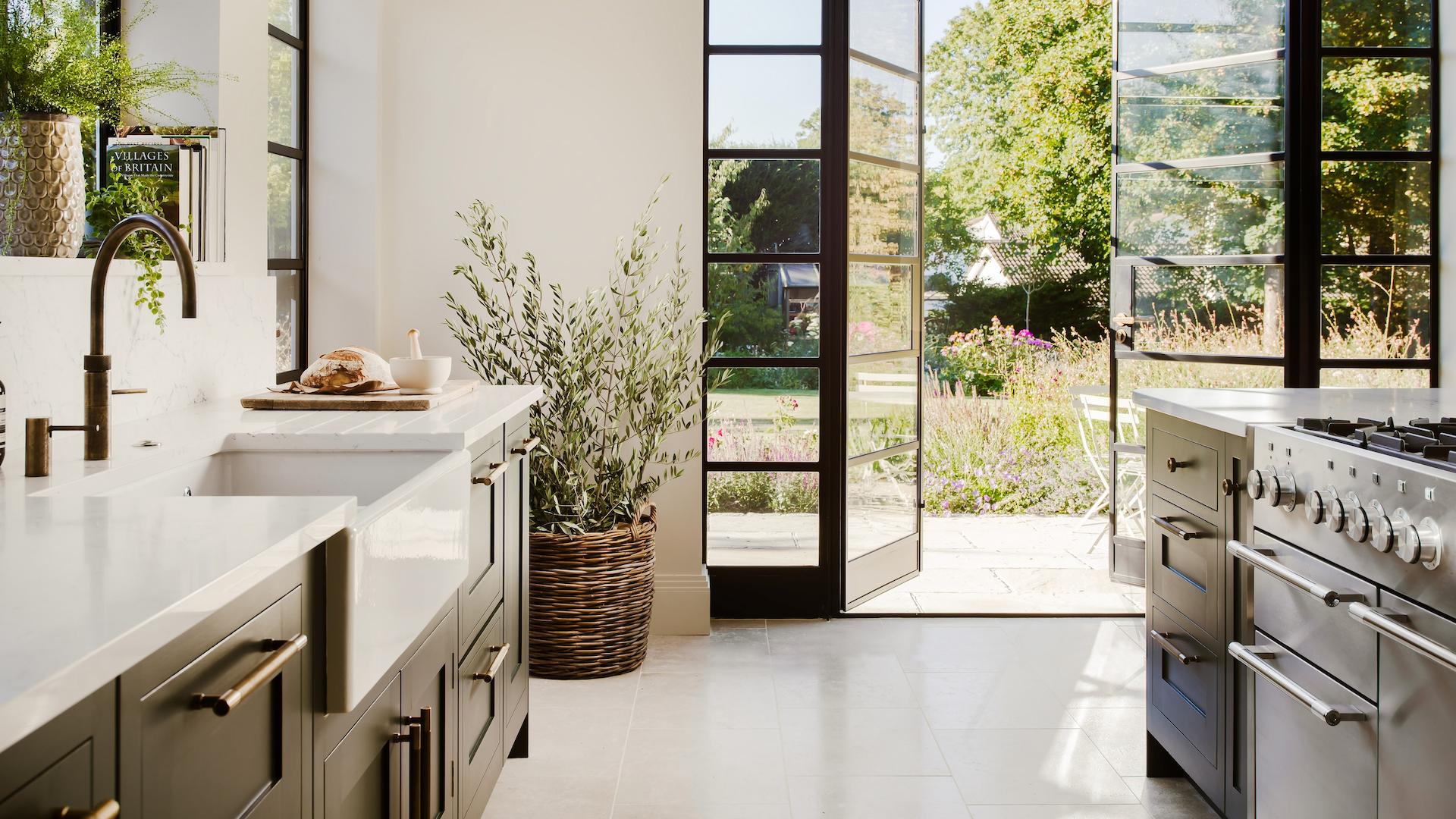 Dark kitchen cabinetry with white worktops with large black framed glass sliding doors