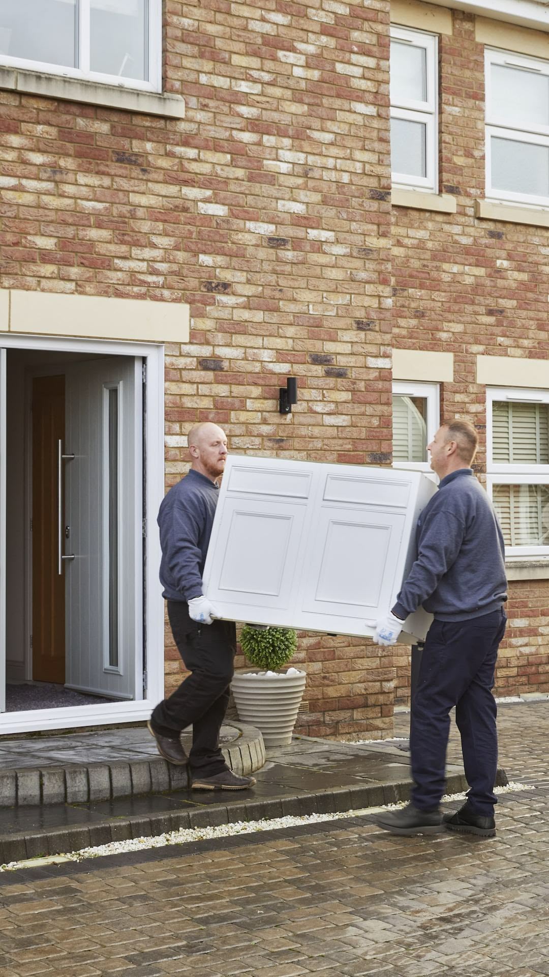 Delivery of Harvey Jones kitchen cabinetry shown by two men carrying a white cabinet door into home entrance
