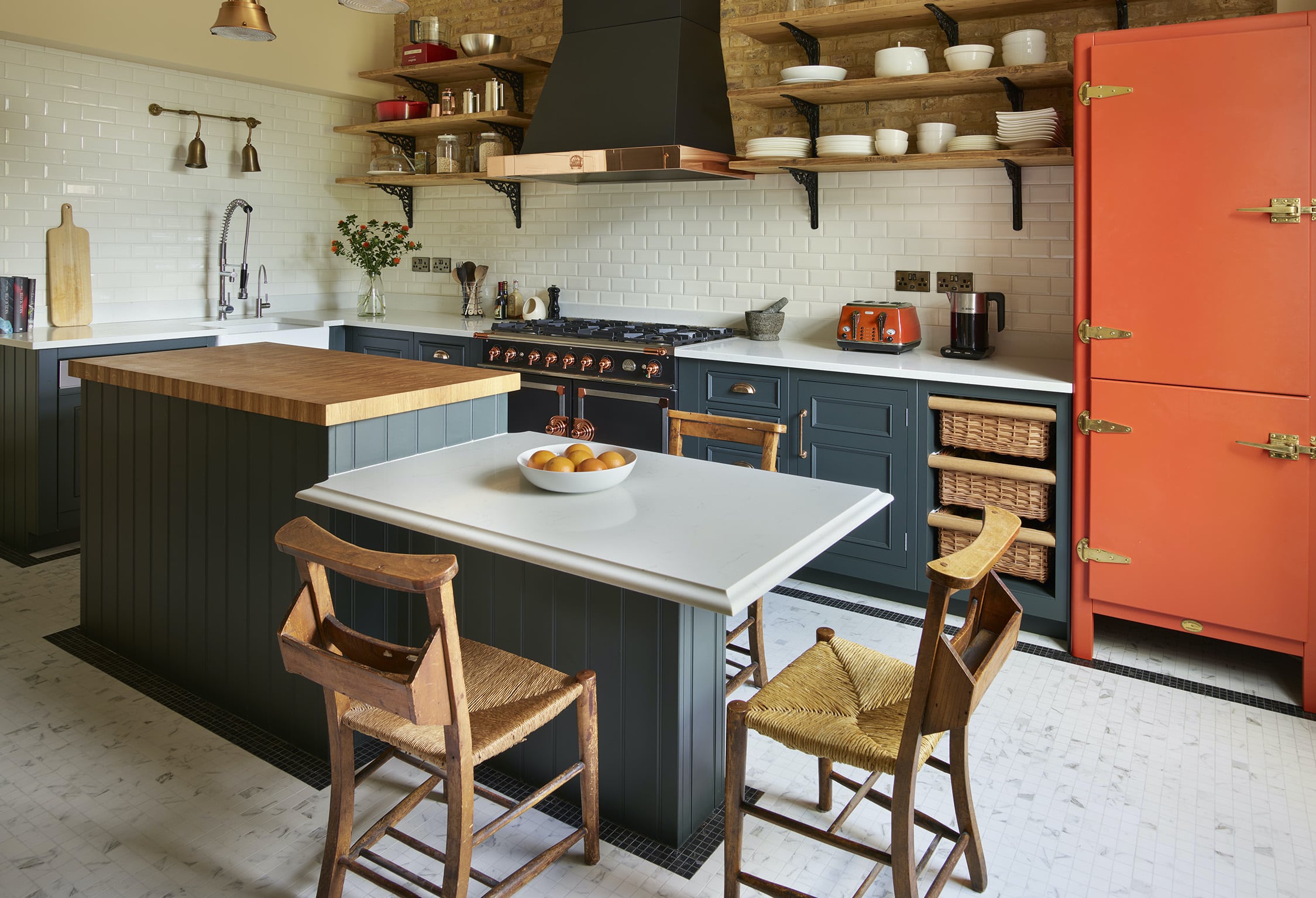 Dark green kitchen cabinetry with white worktops and orange pantry larder