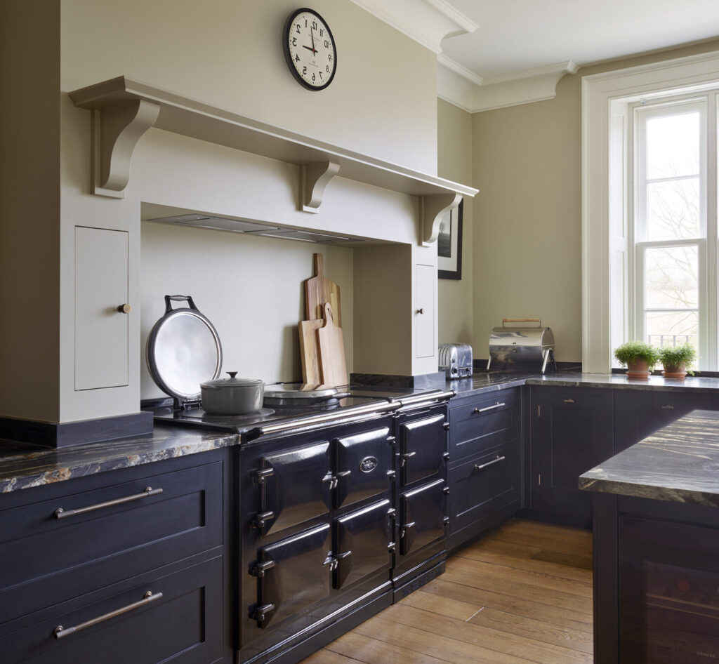 Navy blue kitchen cabinetry around chimney breast alcove with cooker and beige overhead shelving