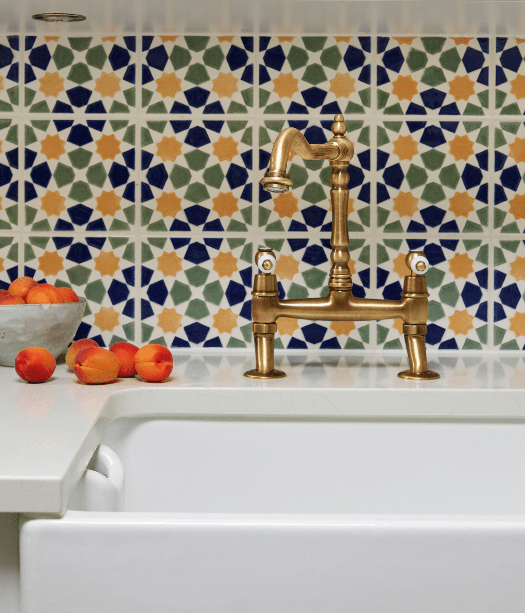 Harvey Jones kitchen appliances and accessories shown by a gold tap over a white basin sink with a decorative tiled splashback