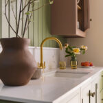 Sage green kitchen cabinetry with white worktops and basin sink with gold tap