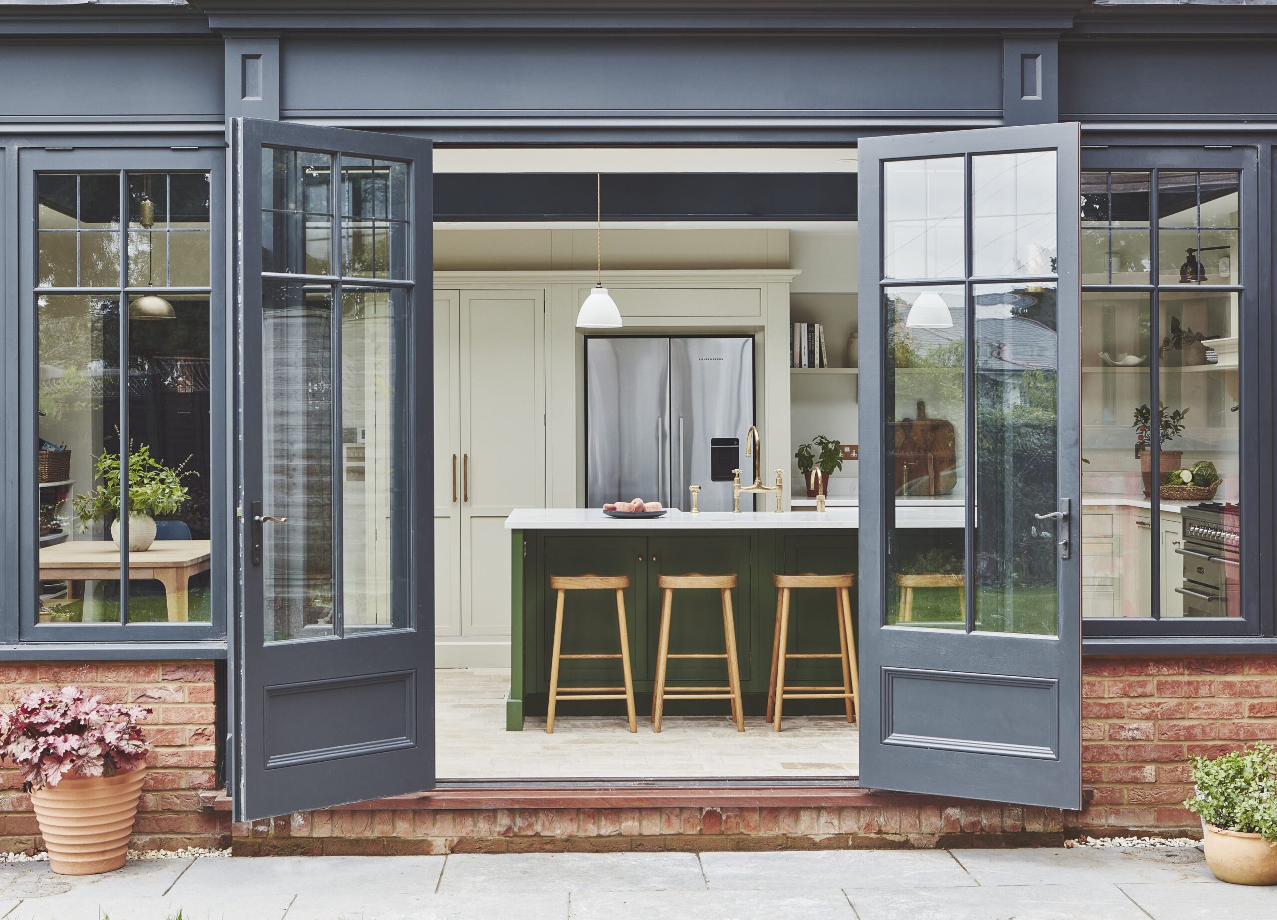 Open French doors looking into an Arbor kitchen featuring a green and white kitchen island with wooden stools