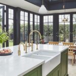 A green kitchen island featuring a white worktop with a white basin sink and gold tap