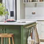 A green kitchen island featuring a white worktop and wooden stool