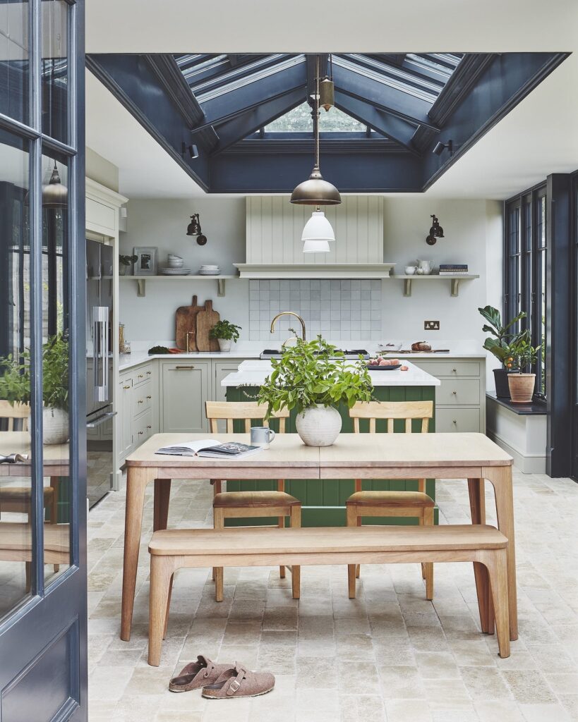 L-shaped kitchen design with pale green kitchen cabinetry and green kitchen island behind open plan dining area