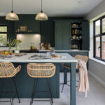 Teal kitchen island featuring a white worktop and wicker stool