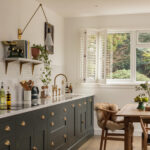 Green Shaker kitchen cabinetry with white worktop and white sink with gold tap next to open plan living area