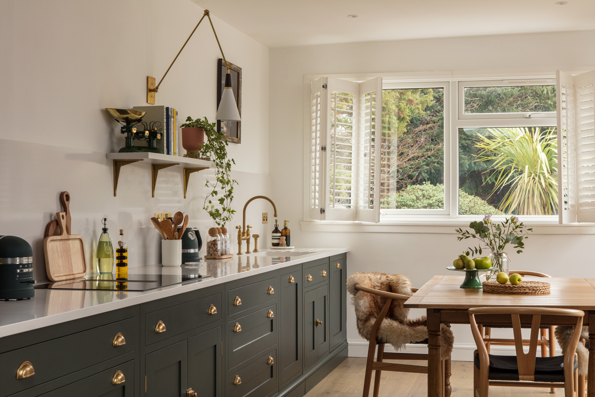 Green Shaker kitchen cabinetry with white worktop and white sink with gold tap next to open plan living area
