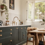 Green Shaker kitchen cabinetry with white worktop and white sink with gold tap next to open plan living area