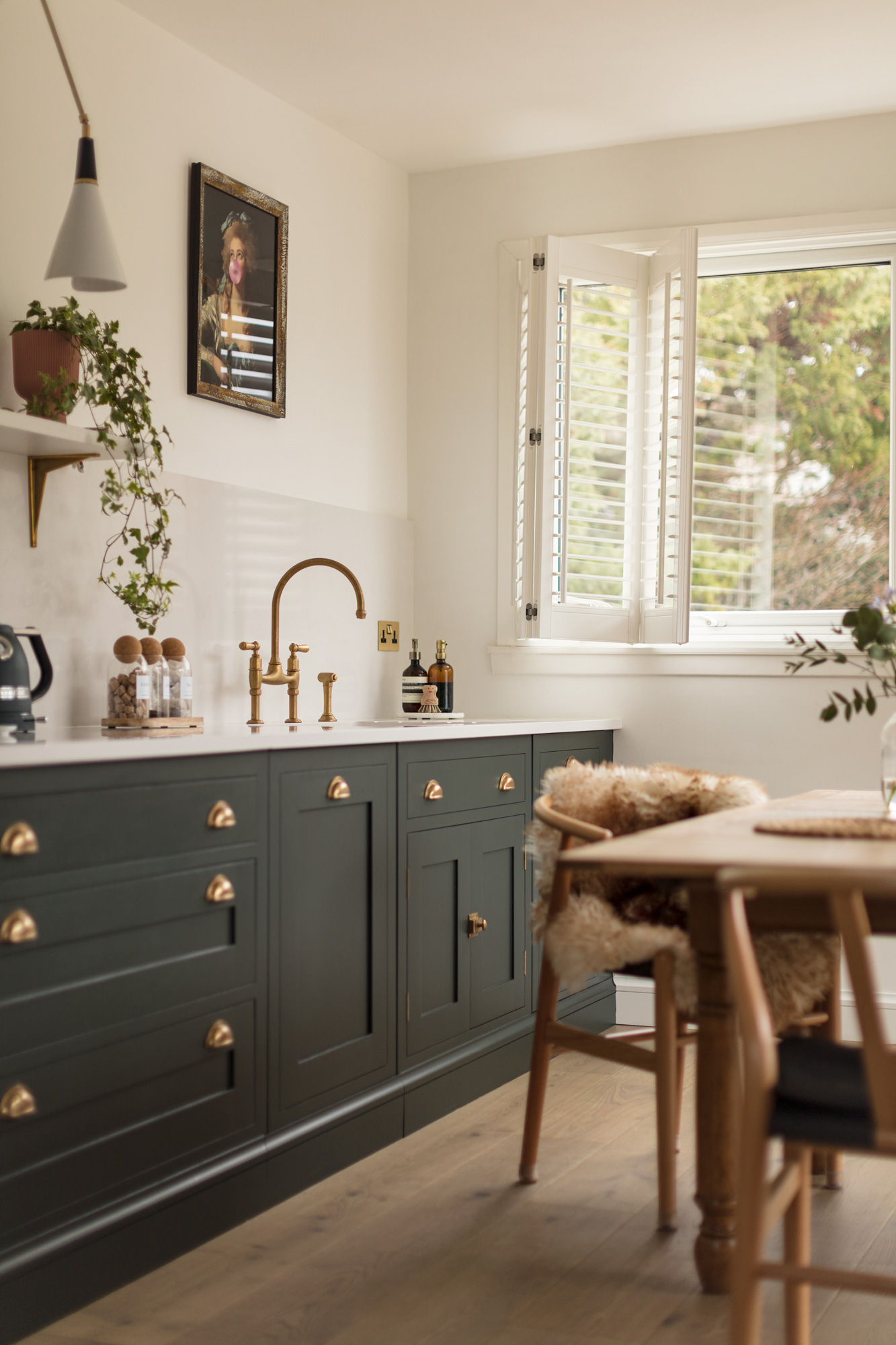 Green Shaker kitchen cabinetry with white worktop and white sink with gold tap next to open plan living area