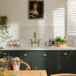 Green Shaker kitchen cabinetry with white worktop and white sink with gold tap