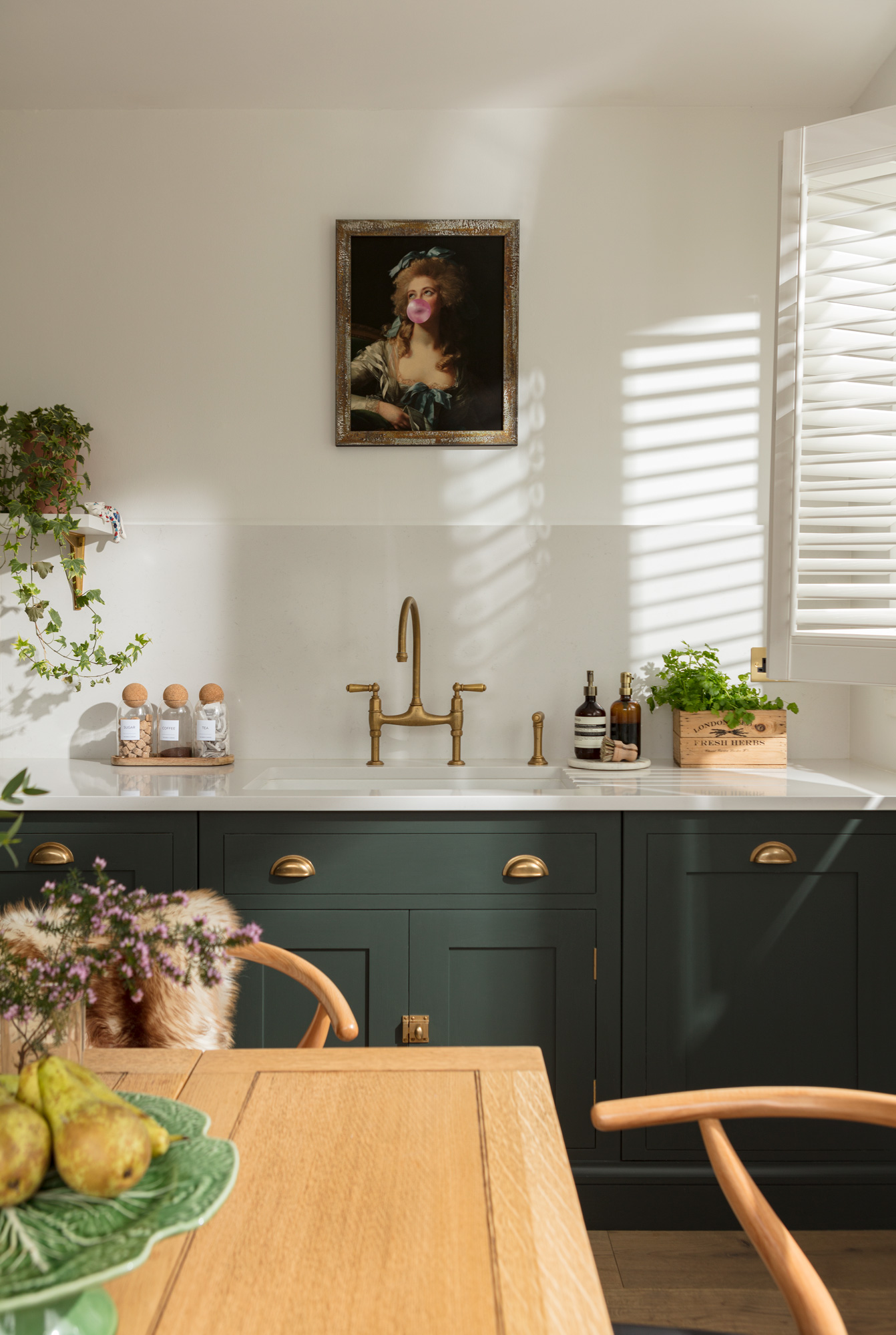 Green Shaker kitchen cabinetry with white worktop and white sink with gold tap