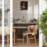 Open plan living area and green Shaker kitchen cabinetry seen through open white glass sliding door