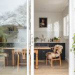 Open plan dining area and green Shaker galley kitchen seen through white framed glass sliding doors