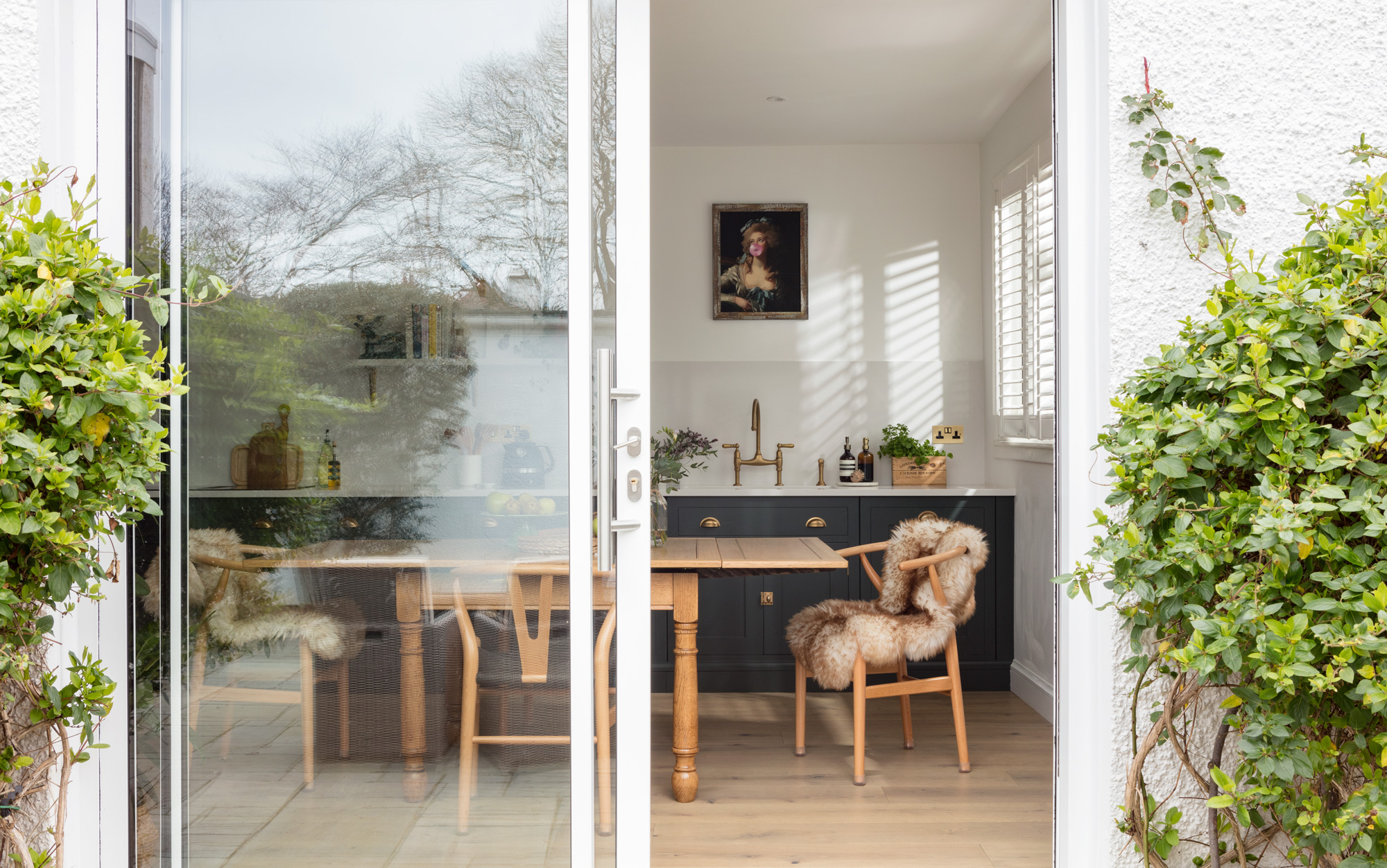 Open plan dining area and green Shaker galley kitchen seen through white framed glass sliding doors