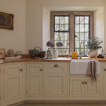 White Original kitchen cabinetry with white sink and brass tap against wooden framed windows