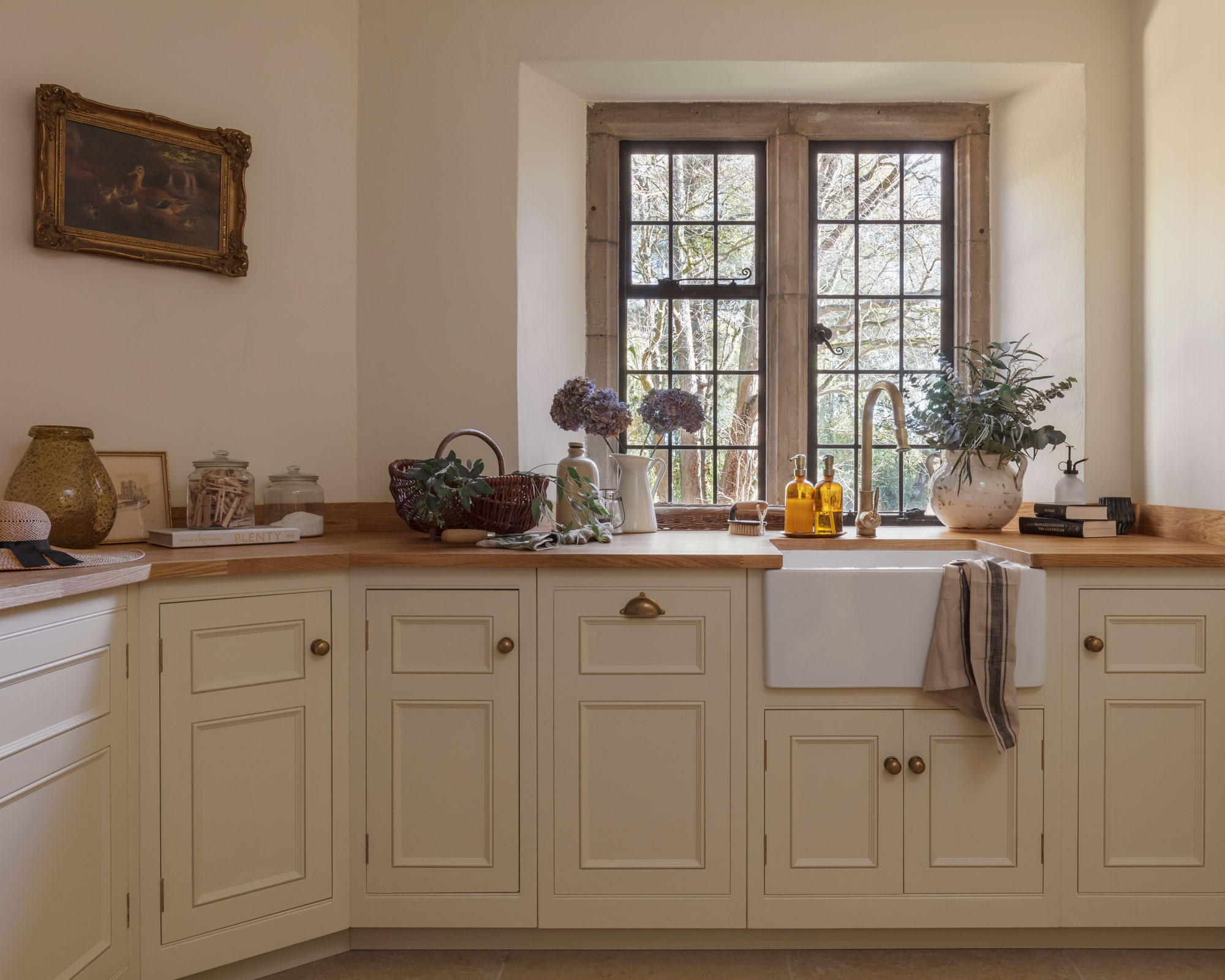White Original kitchen cabinetry with white sink and brass tap against wooden framed windows
