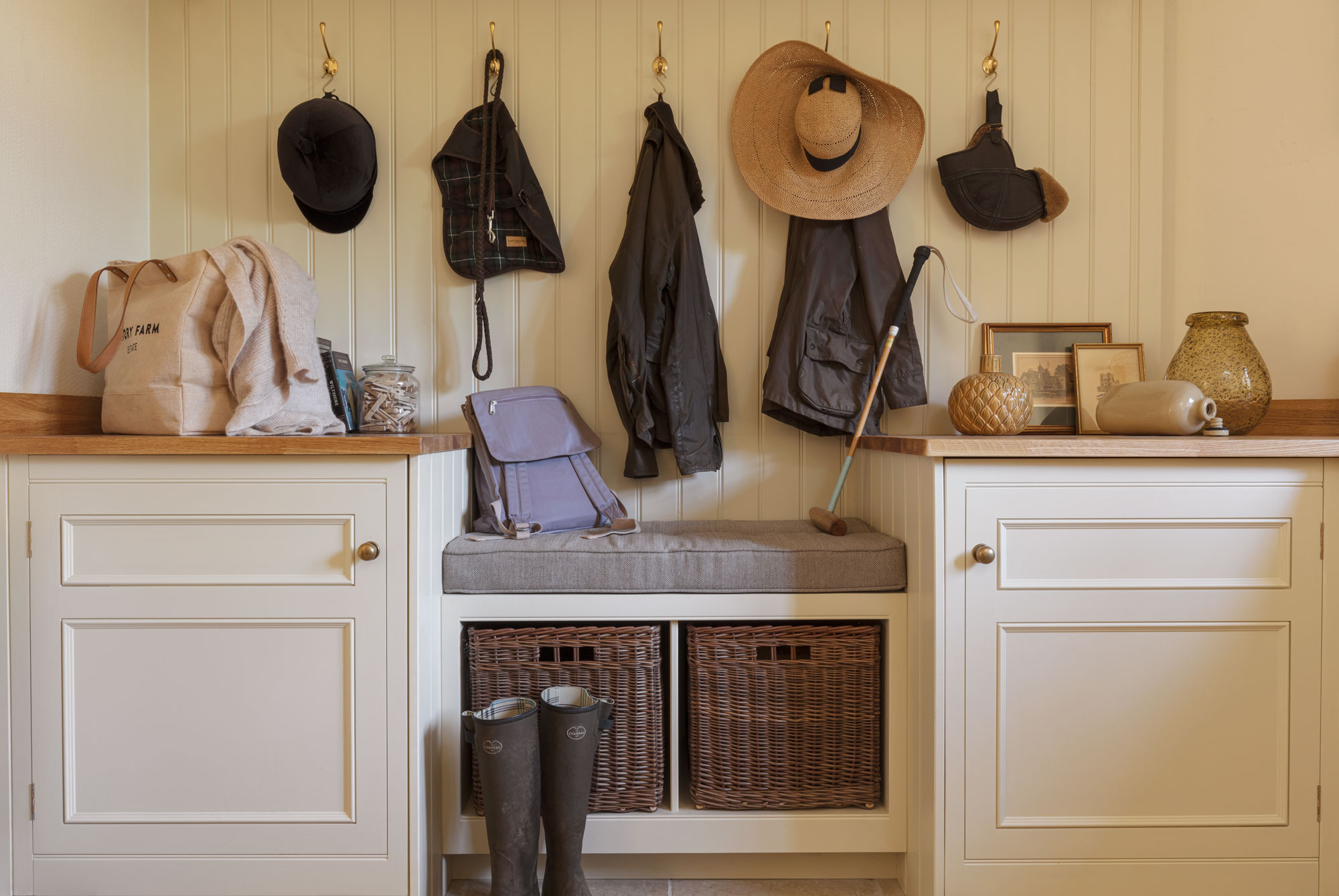 Cream and white boot room featuring grey bench seating, brown storage baskets and coat hooks above