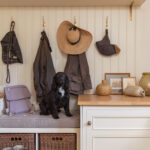 Cream and white boot room featuring grey bench seating, brown storage baskets and coat hooks above