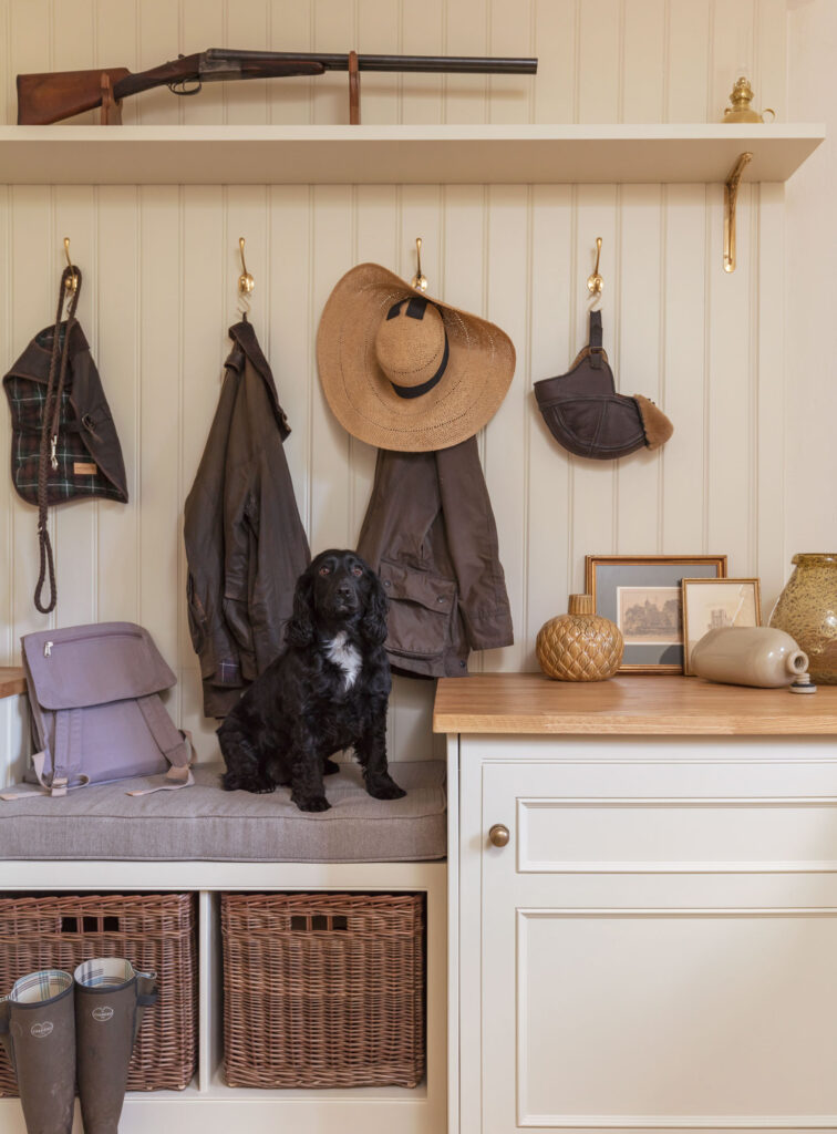 Cream and white boot room featuring grey bench seating, brown storage baskets and coat hooks above