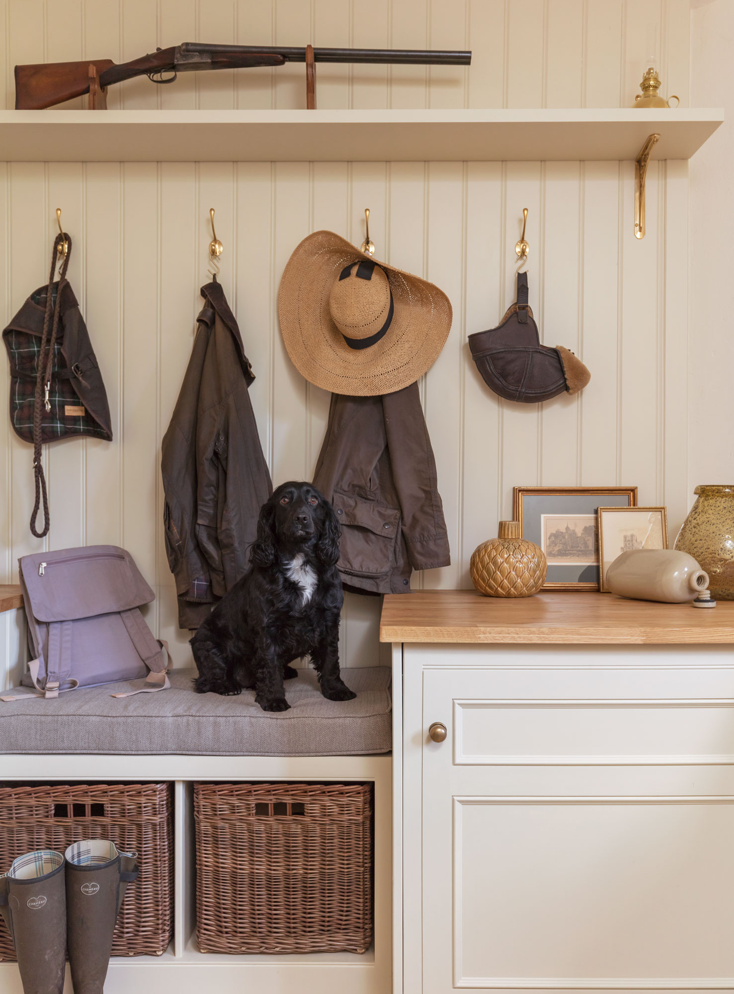 Cream and white boot room featuring grey bench seating, brown storage baskets and coat hooks above