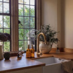 White Original kitchen cabinetry with white sink and brass tap against wooden framed windows