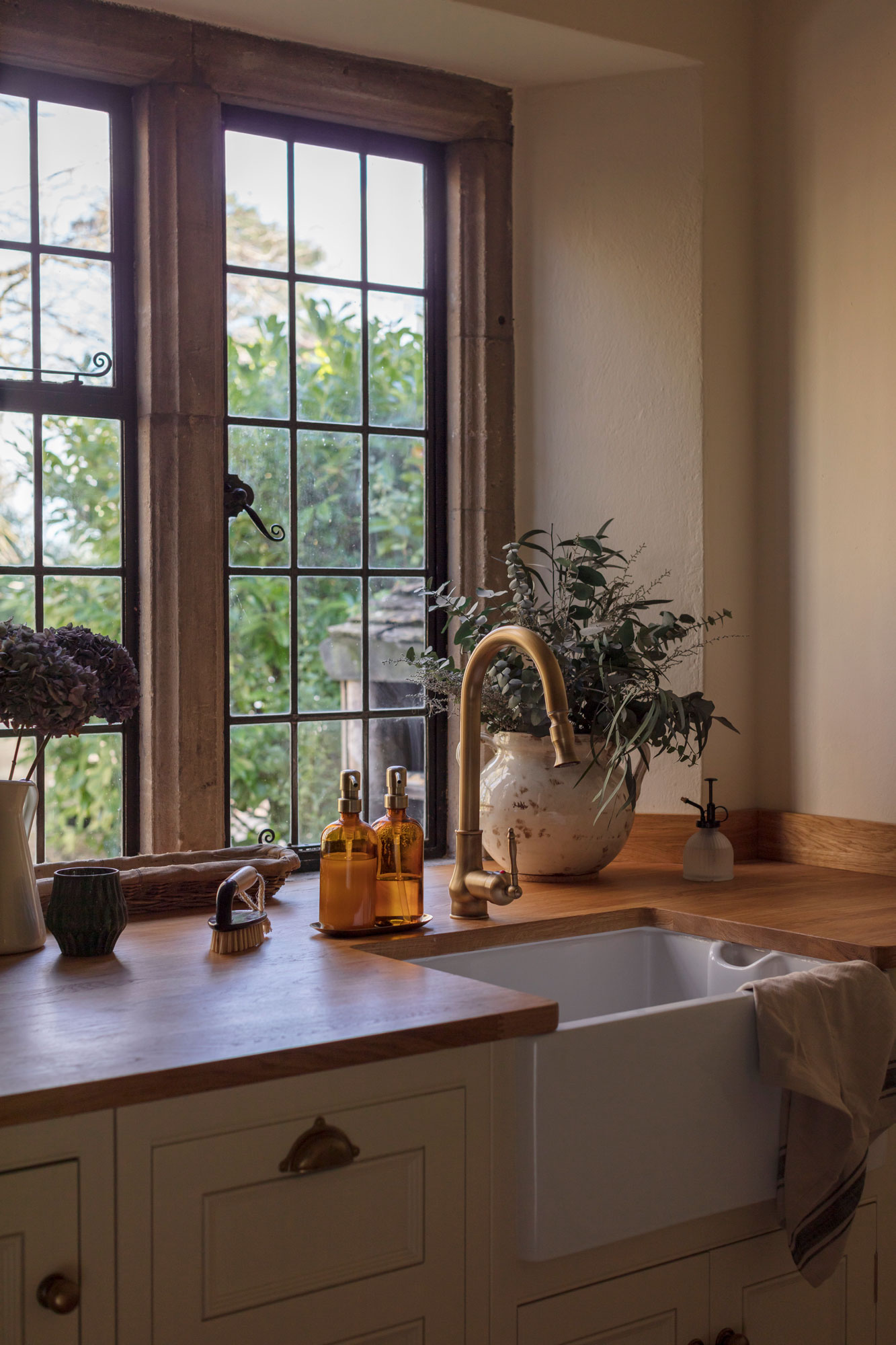 White Original kitchen cabinetry with white sink and brass tap against wooden framed windows