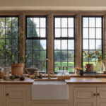 White Original kitchen cabinetry with white sink and brass tap against wooden framed windows
