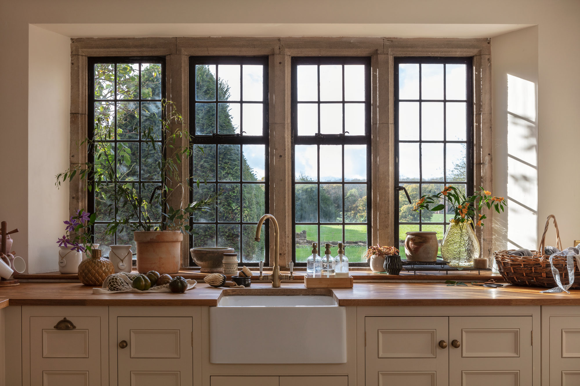 White Original kitchen cabinetry with white sink and brass tap against wooden framed windows
