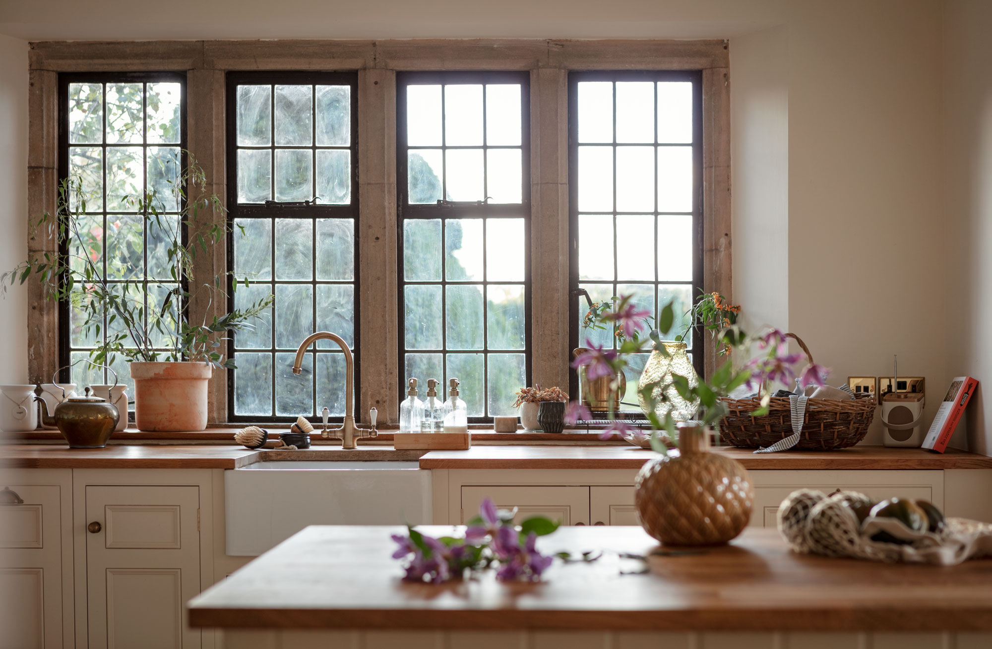 White Original kitchen cabinetry with white sink and brass tap against wooden framed windows