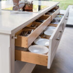 White Shaker kitchen island with open drawers revealing oak interior and organised crockery