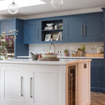 White Shaker kitchen island with white worktop and integrated wine fridge overlooking blue kitchen cabinetry