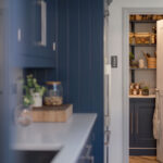 Blue Shaker kitchen cabinetry next to walk-in pantry with white door