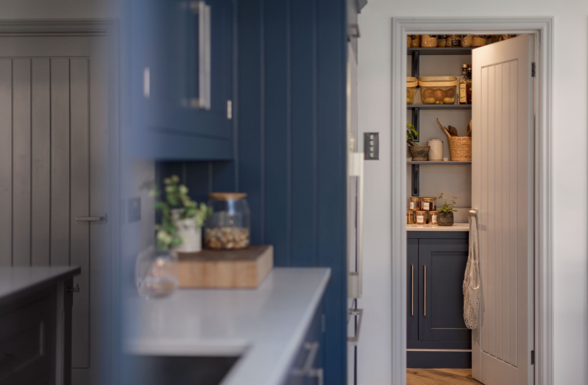 Blue Shaker kitchen cabinetry next to walk-in pantry with white door