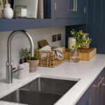 Blue Shaker kitchen cabinetry with white worktop featuring integrated sink with silver tap and overhead shelving