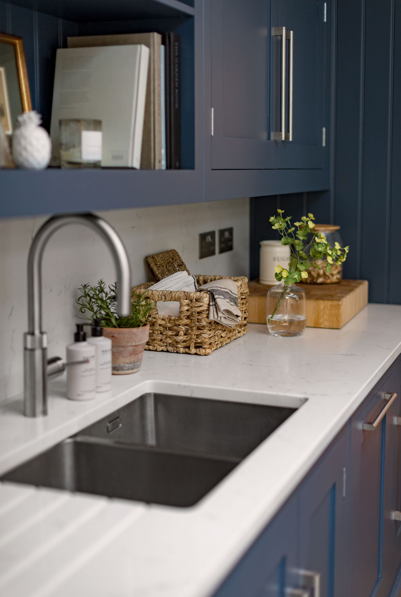 Blue Shaker kitchen cabinetry with white worktop featuring integrated sink with silver tap and overhead shelving
