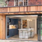 External view of navy Shaker kitchen with white kitchen island seen through open large glass sliding door